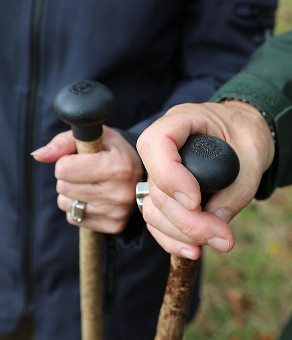 Two people holding two caster seed walking sticks engraved with a family crest