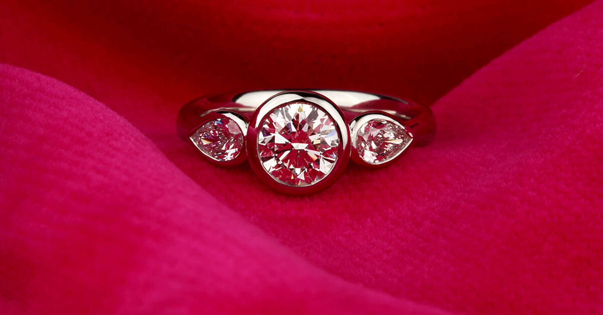 A three stone engagement diamond ring on a pink fabric background