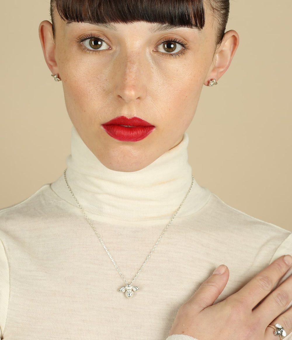 a women with red lipstick wearing a bumblebee necklace and ring in silver.